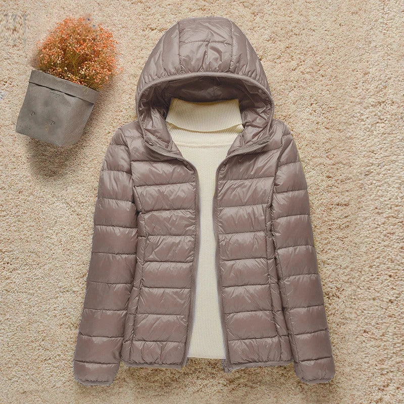Giacca invernale trapuntata da donna con cappuccio, colore grigio, su sfondo beige. Moda femminile, abbigliamento caldo, stile casual.