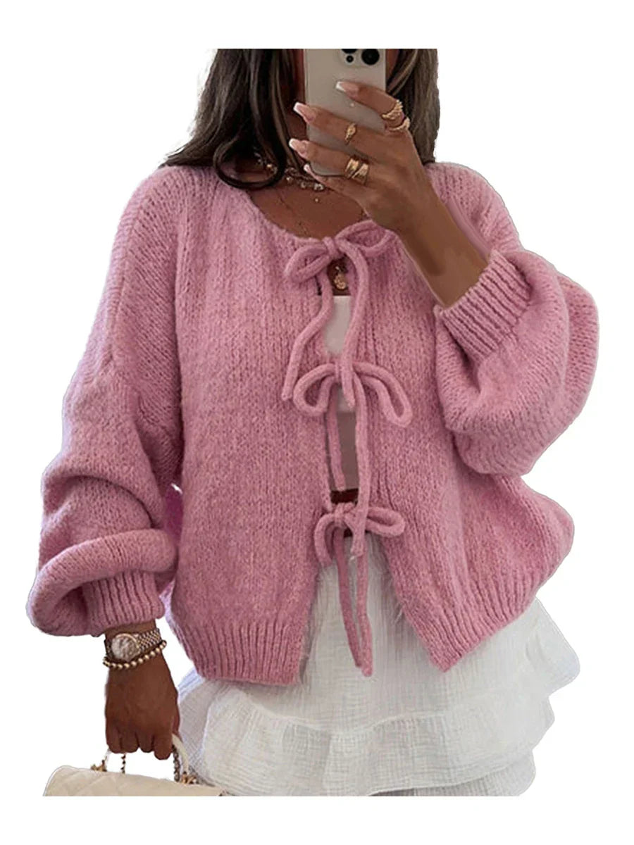 Cardigan rosa in maglia con fiocchi, maniche lunghe e design morbido, indossato su top bianco. Moda donna, abbigliamento autunnale elegante.