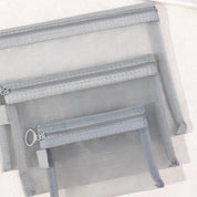 Set di tre pochette trasparenti in rete grigia con cerniera, ideali per organizzare cosmetici e accessori da viaggio. Design pratico e versatile.