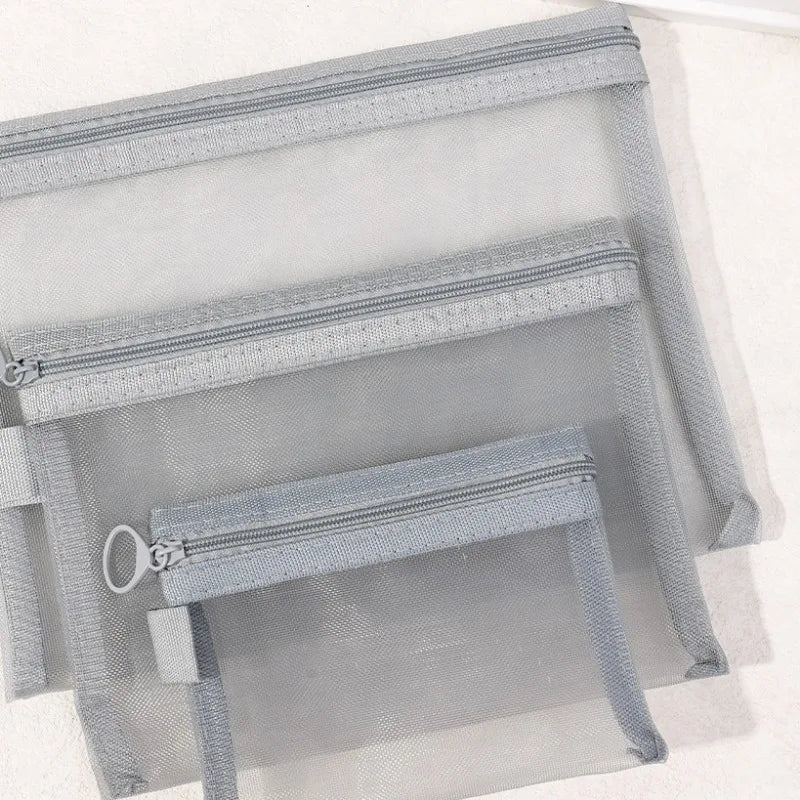 Set di tre pochette trasparenti in rete grigia con cerniera, ideali per organizzare cosmetici e accessori da viaggio. Design pratico e versatile.