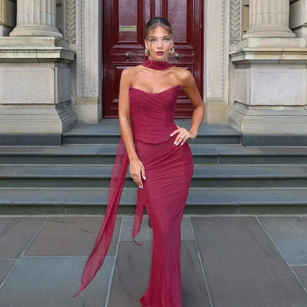 Abito da sera elegante rosso bordeaux, lungo e aderente, con sciarpa abbinata, indossato da modella su gradini di edificio storico.