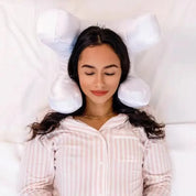 Donna che dorme su cuscino ergonomico bianco a forma di osso, indossa pigiama a righe rosa. Comfort, supporto cervicale, riposo notturno.