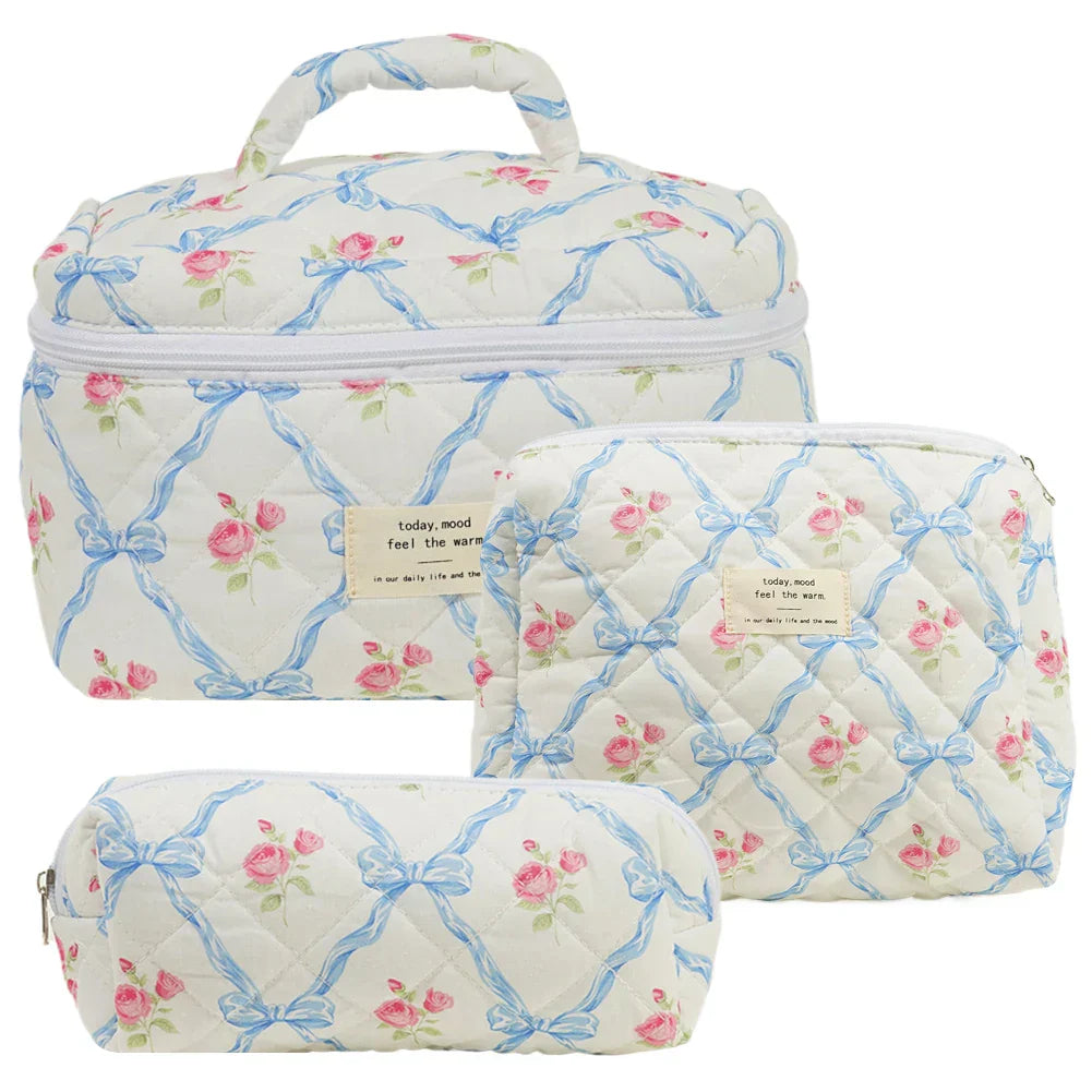 Set di tre beauty case trapuntati con motivo floreale e fiocchi blu, ideali per viaggi. Include borsa grande, media e piccola con cerniera.