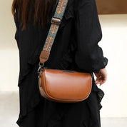 Borsa a tracolla in pelle marrone con cinghia decorata, indossata da una persona in abito nero. Accessorio moda elegante e versatile.
