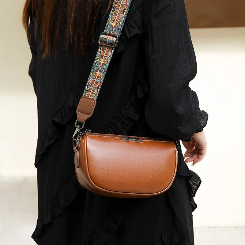 Borsa a tracolla in pelle marrone con cinghia decorata, indossata da una persona in abito nero. Accessorio moda elegante e versatile.
