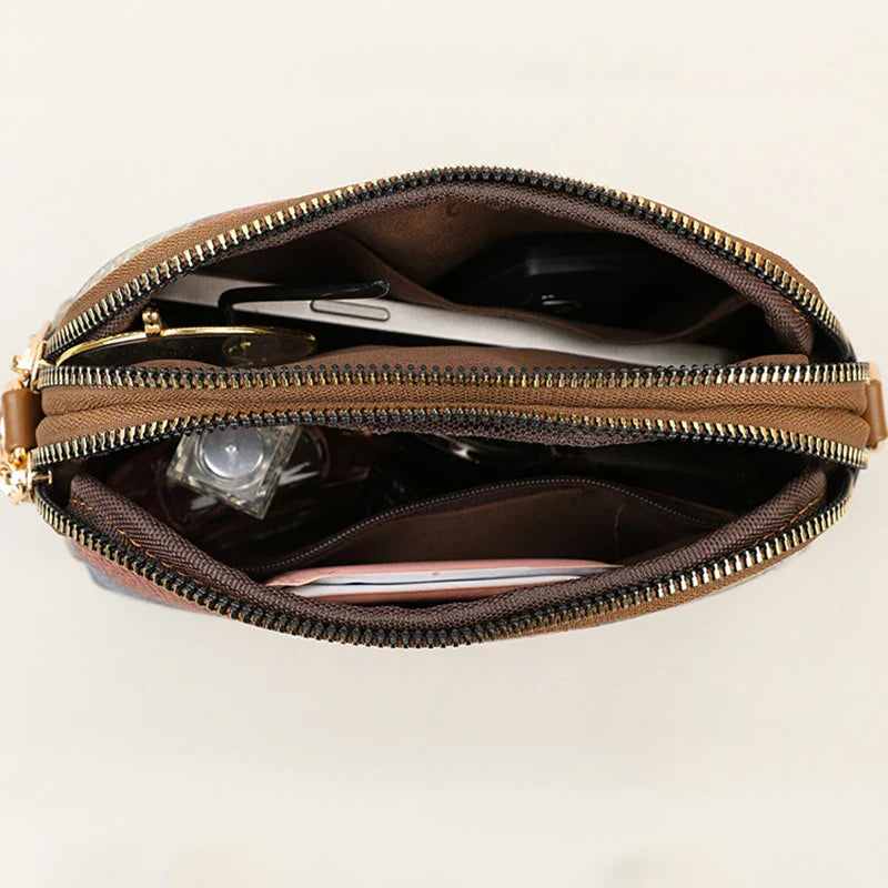 Borsa a tracolla in pelle marrone con cerniera aperta, mostra scomparti interni con smartphone, chiavi e accessori. Design elegante e funzionale.