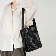 Borsa a tracolla nera in pelle trapuntata, indossata da una persona con camicia bianca. Design elegante e moderno, ideale per moda urbana.