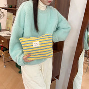 Donna con maglione verde menta tiene borsa a righe gialle e blu. Moda invernale, accessori colorati, stile casual chic.