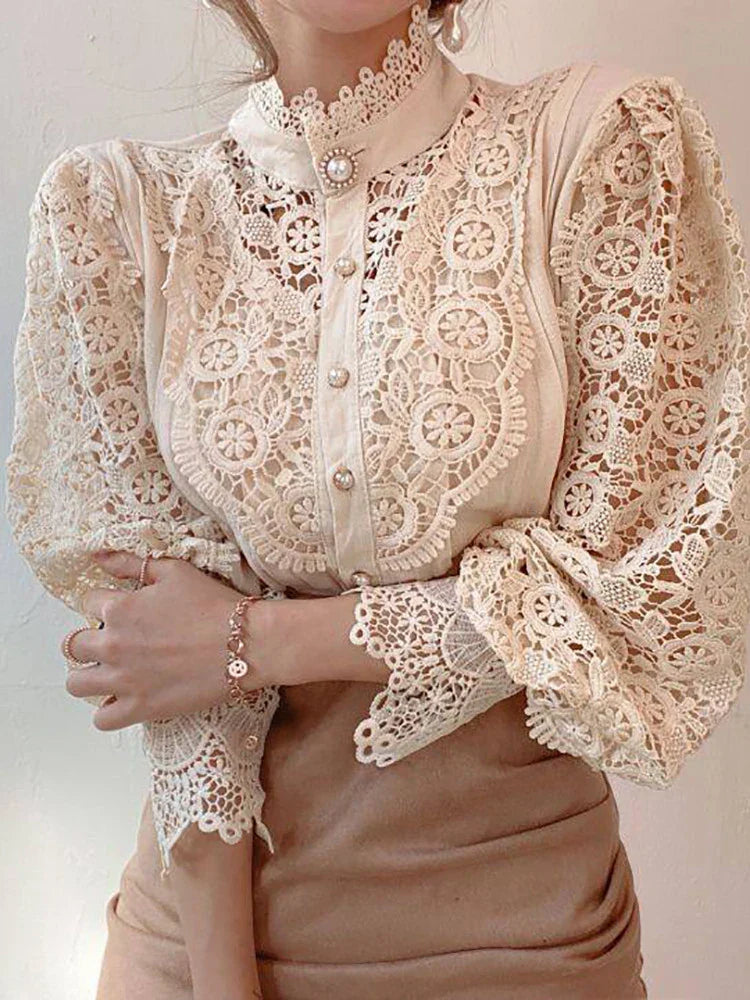Blusa elegante in pizzo beige con maniche lunghe e dettagli floreali, colletto alto e bottoni decorativi. Moda femminile raffinata e chic.