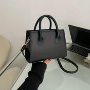 Borsa a mano nera in pelle su tavolo con laptop, design elegante e minimalista, perfetta per moda donna, accessorio versatile e chic.