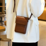 Borsa a tracolla in pelle marrone su giacca bianca, design elegante e minimalista, accessorio moda uomo/donna, perfetta per uso quotidiano.