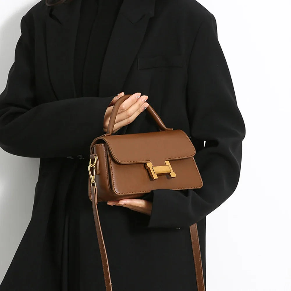 Borsa a tracolla marrone in pelle con chiusura dorata, indossata da una persona in cappotto nero. Elegante accessorio moda donna.