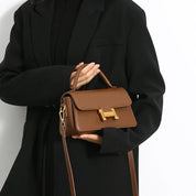 Borsa a tracolla marrone in pelle con chiusura dorata, indossata da una persona in cappotto nero. Elegante accessorio moda donna.