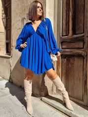 Donna con abito blu a pieghe e stivali beige, posa su strada cittadina. Moda autunnale, abbigliamento casual chic, tendenza abiti corti.