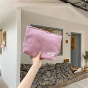 Borsa a mano rosa in tessuto a coste, tenuta da una mano, davanti a una casa moderna. Accessorio moda femminile, elegante e pratico.