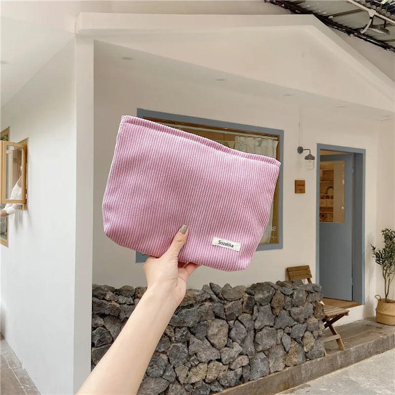 Borsa a mano rosa in tessuto a coste, tenuta da una mano, davanti a una casa moderna. Accessorio moda femminile, elegante e pratico.