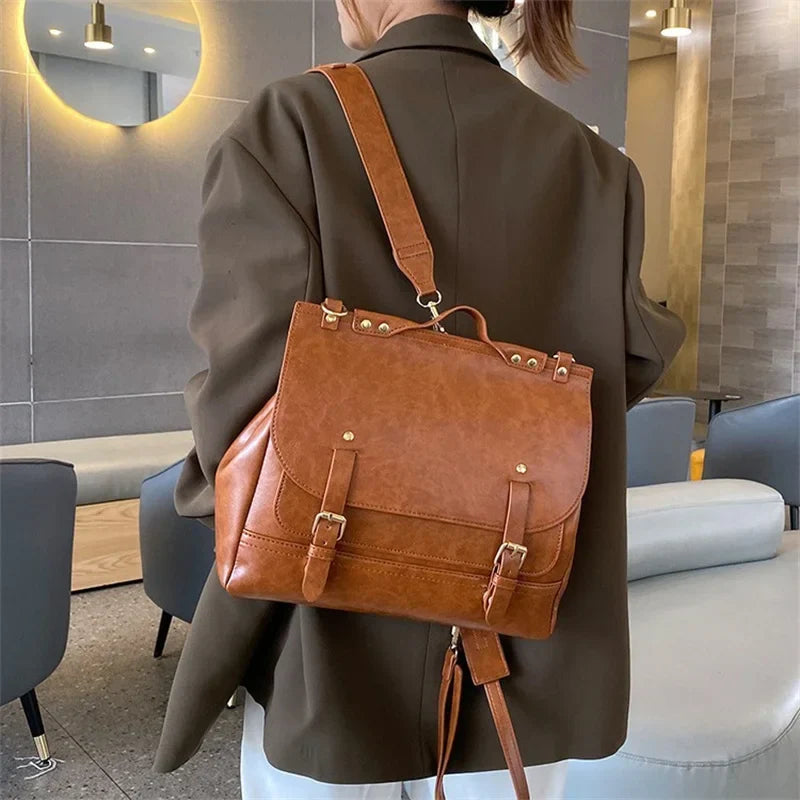 Zaino in pelle marrone elegante, indossato da una persona in giacca scura, in un ambiente moderno. Design con fibbie e dettagli dorati.