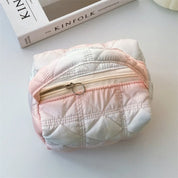 Borsa cosmetica trapuntata rosa e bianca con cerniera dorata, su tavolo bianco accanto a rivista Kinfolk. Accessorio moda elegante e pratico.