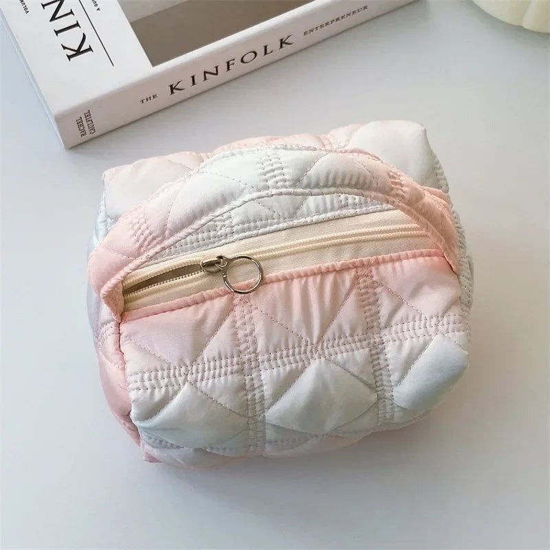 Borsa cosmetica trapuntata rosa e bianca con cerniera dorata, su tavolo bianco accanto a rivista Kinfolk. Accessorio moda elegante e pratico.