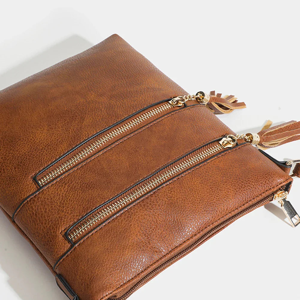 Borsa a tracolla in pelle marrone con doppie cerniere dorate e nappine. Design elegante e pratico, ideale per moda donna e accessori.