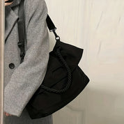 Cappotto grigio con borsa a tracolla nera in tessuto, design elegante e moderno, ideale per moda autunno inverno. Accessorio versatile e chic.