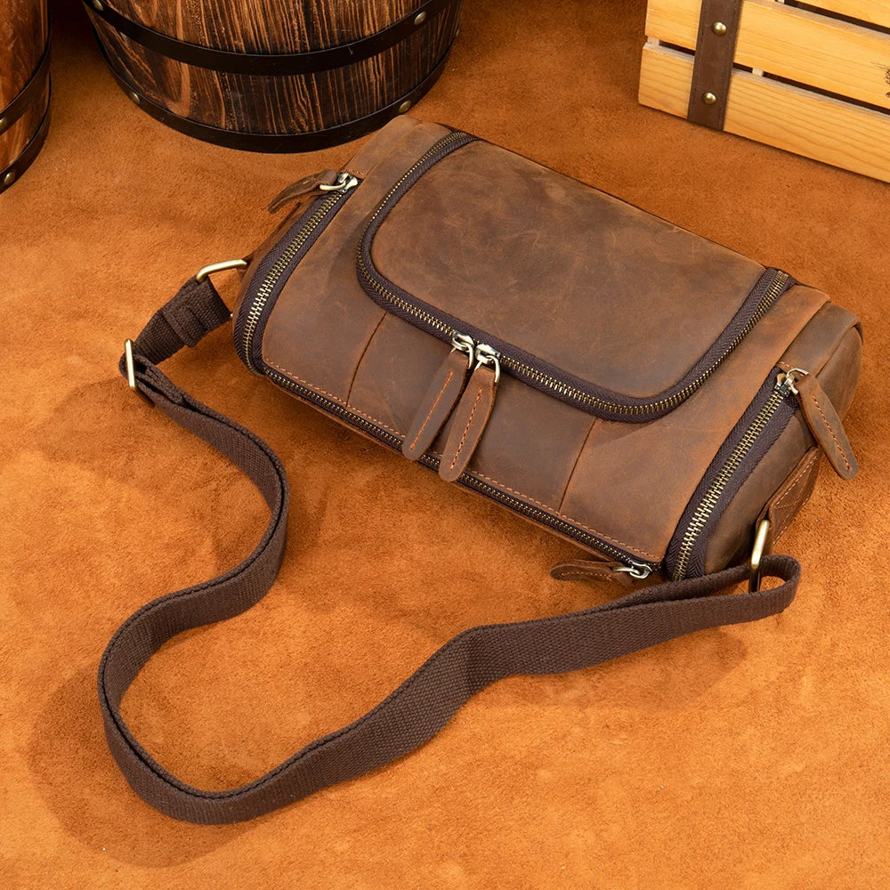 Borsa a tracolla in pelle marrone vintage su sfondo marrone, con cerniere e tasche multiple. Accessorio moda uomo elegante e funzionale.