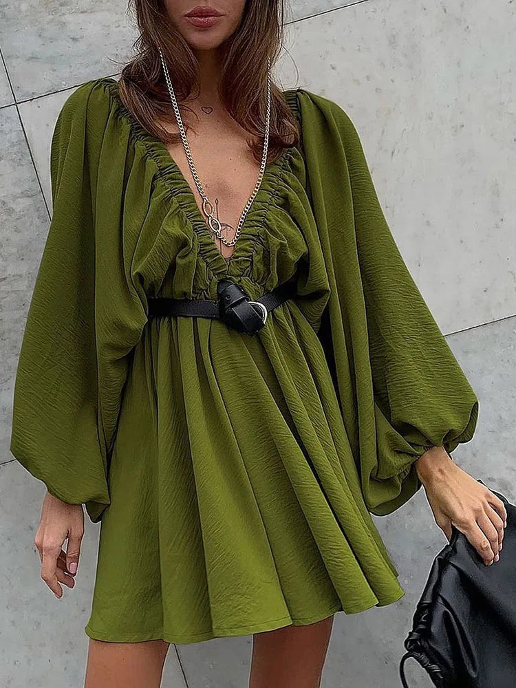 Abito corto verde oliva con maniche a sbuffo, scollo a V arricciato, cintura nera e collana lunga. Moda donna elegante e trendy.