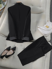 Completo nero elegante da donna su divano beige, con giacca e pantaloni. Scarpe nere a punta e borsa bianca a tracolla. Moda femminile formale.
