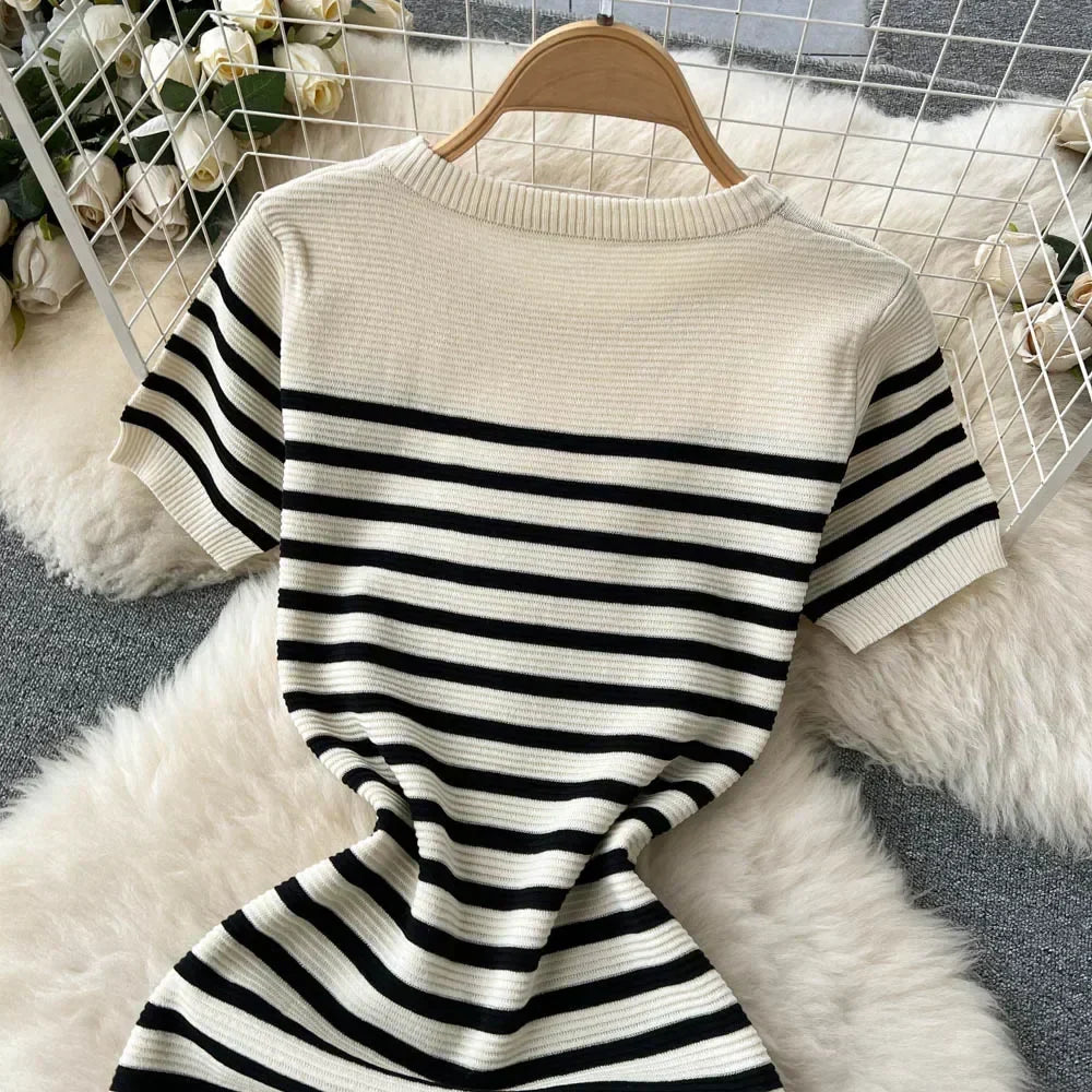Maglia a righe bianche e nere su sfondo peloso, appesa su gruccia. Design casual, tessuto a coste, ideale per moda autunnale.