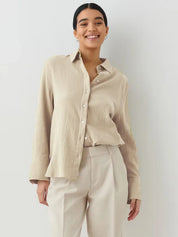 Donna sorridente con camicia beige a maniche lunghe e pantaloni chiari. Moda casual elegante, abbigliamento femminile, stile minimalista.