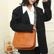Donna con borsa a tracolla in pelle marrone, indossa giacca nera e camicia bianca. Accessorio moda elegante, perfetto per look casual e formali.