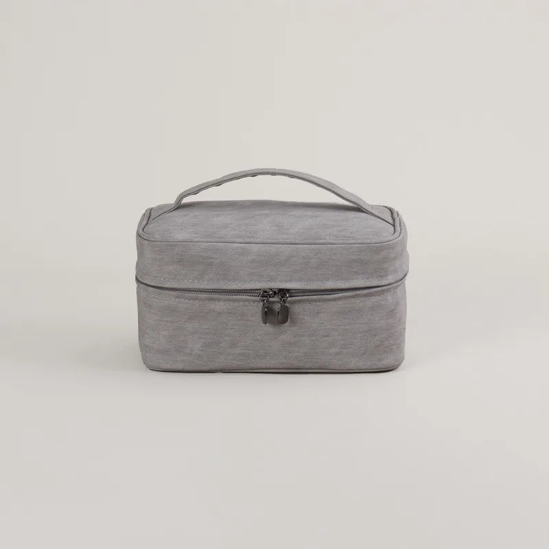 Borsa da viaggio grigia con manico, design compatto e chiusura a zip. Ideale per organizzare accessori e cosmetici. Elegante e funzionale.