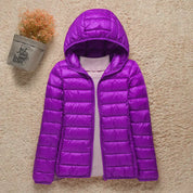Giacca piumino viola con cappuccio, design trapuntato, su sfondo beige. Moda invernale donna, abbigliamento caldo e leggero.