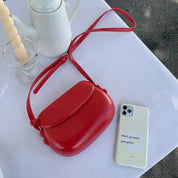 Borsa a tracolla rossa su tavolo bianco accanto a smartphone bianco e caffettiera; accessori moda eleganti, design moderno, stile minimalista.