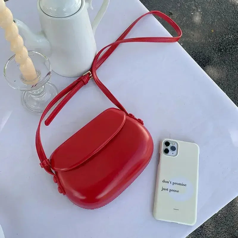 Borsa a tracolla rossa su tavolo bianco accanto a smartphone bianco e caffettiera; accessori moda eleganti, design moderno, stile minimalista.