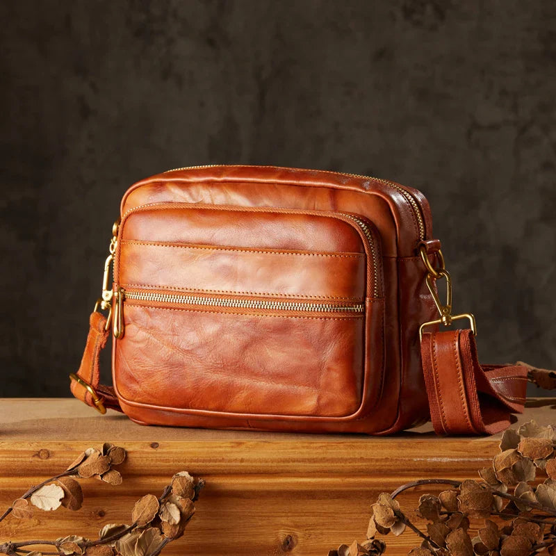 Borsa a tracolla in pelle marrone su tavolo di legno, design elegante e vintage, con cerniere dorate. Accessorio moda uomo/donna.