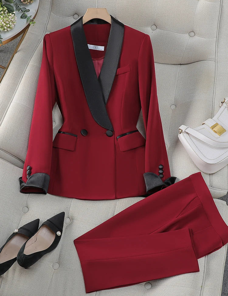 Completo da donna elegante rosso con giacca a doppio petto e pantaloni, dettagli neri, su divano beige. Scarpe nere e borsa bianca accanto.