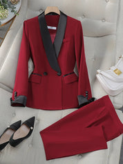 Completo da donna elegante rosso con giacca a doppio petto e pantaloni, dettagli neri, scarpe nere a punta, borsa bianca su divano beige.