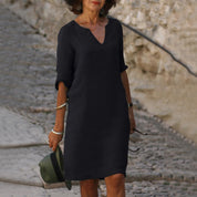 Donna con abito nero elegante, maniche a tre quarti, in strada acciottolata. Moda femminile, abbigliamento casual chic, accessori minimal.