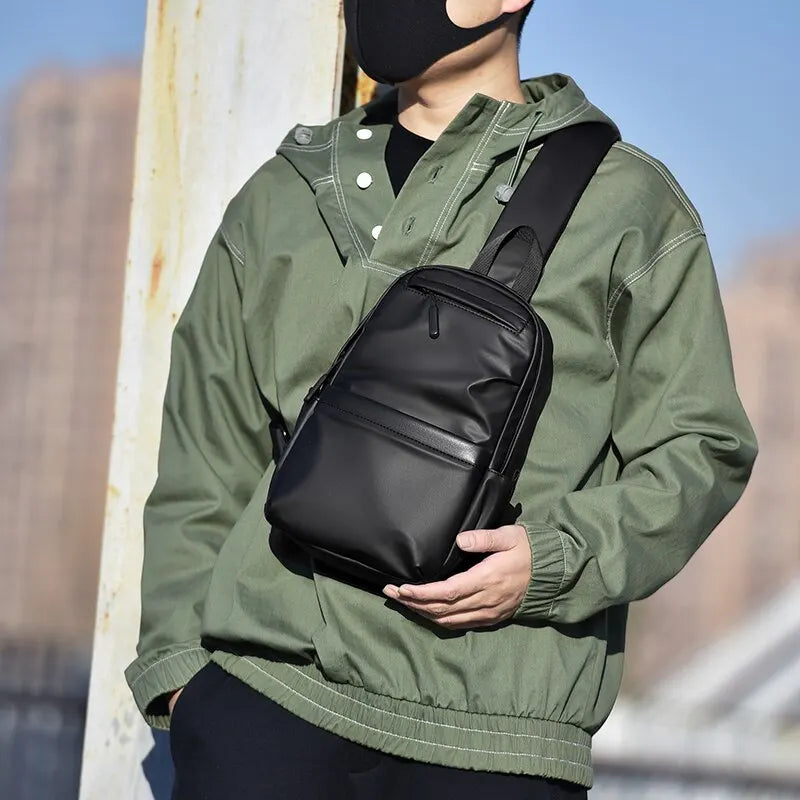 Uomo con giacca verde indossa zaino a tracolla nero in pelle, stile urbano. Accessorio moda maschile, pratico per viaggi e uso quotidiano.