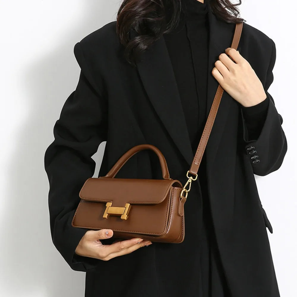 Borsa a tracolla marrone in pelle con chiusura dorata, indossata da una donna in cappotto nero. Elegante accessorio moda femminile.