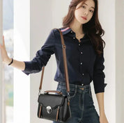 Donna con camicia blu e jeans, indossa una borsa a tracolla nera elegante. Moda femminile, accessori di tendenza, stile casual chic.