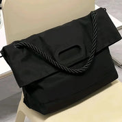 Borsa a tracolla nera su sedia, design moderno con manico intrecciato. Accessorio elegante per moda femminile, ideale per lavoro e tempo libero.