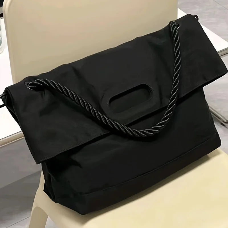 Borsa a tracolla nera su sedia, design moderno con manico intrecciato. Accessorio elegante per moda femminile, ideale per lavoro e tempo libero.