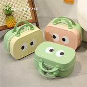 Tre valigie colorate con occhi disegnati, in verde e beige, su pavimento grigio. Design giocoso, perfette per viaggi brevi o bambini.