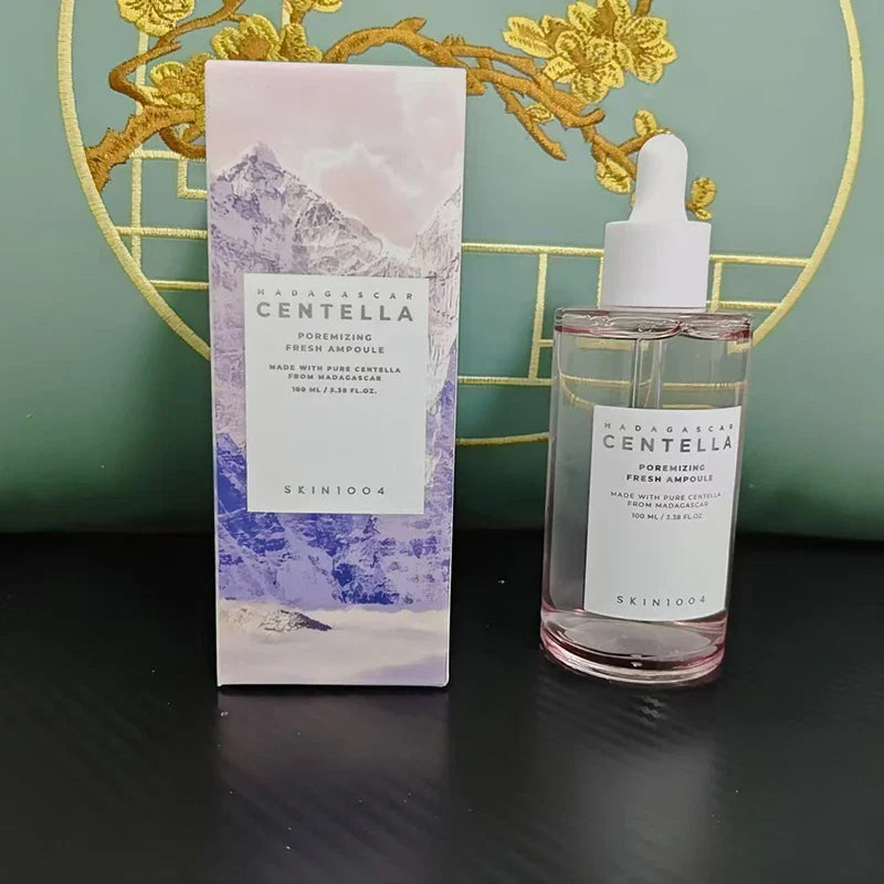 Boccetta di siero viso Skin1004 Madagascar Centella, 100 ml, con scatola decorata da montagne e fiori gialli, su sfondo verde.