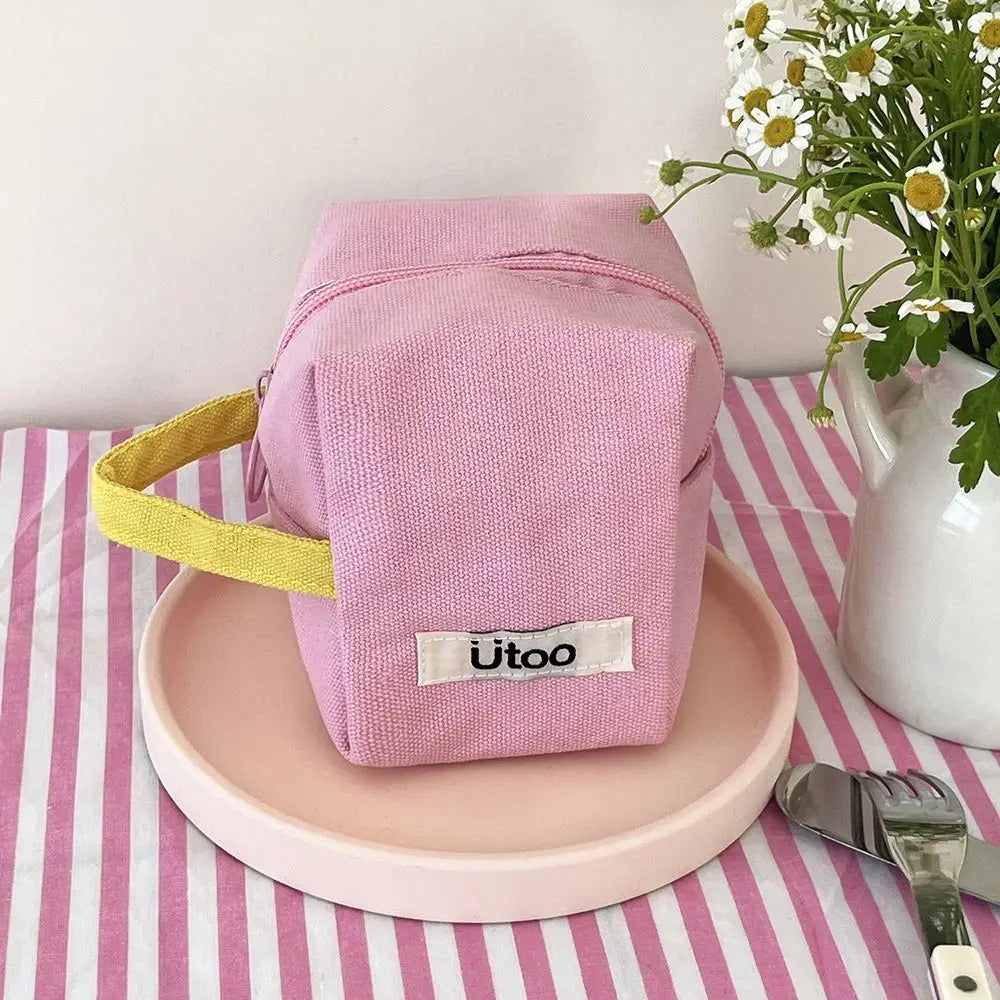 Astuccio rosa in tessuto con manico giallo su piatto rosa, decorato con fiori bianchi e verdi. Accessorio moda, design elegante e funzionale.