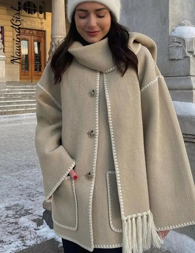 Donna con cappotto beige invernale con cappuccio e frange, davanti a edificio storico. Moda inverno, abbigliamento caldo, stile elegante.