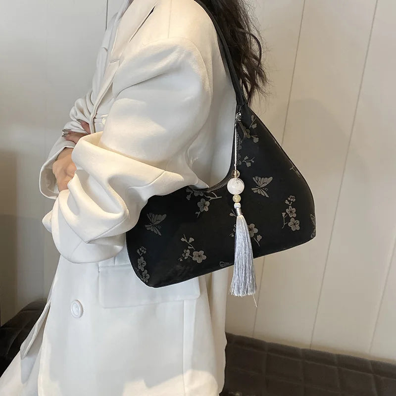 Borsa a spalla nera con motivo floreale, decorata con nappina bianca. Accessorio moda elegante per donna, perfetto per look casual e formali.