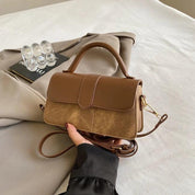 Borsa a tracolla in pelle marrone su giacca beige, design elegante, manico superiore, chiusura a patta, accessorio moda donna, stile casual chic.